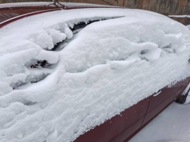 Kar yağışı kışın bulutlu geçen kar fırtınasından sonra park halindeki kırmızı bir arabanın yan ve arka tarafına yerleşmiş.