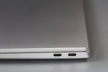 İnce gümüş çantadaki katlanmış dizüstü bilgisayarın bir parçası. Gri bir yüzeyde C tipi, seçici odak noktasında yakın plan.