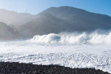 Dağdan süzülen güneş ışınlarıyla kumsalda büyük dalgalar kopuyor.