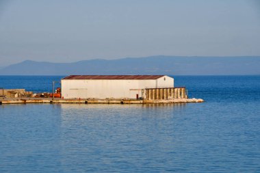 Gün batımında sakin denizin ortasındaki bir rıhtımda küçük bir yük deposu.