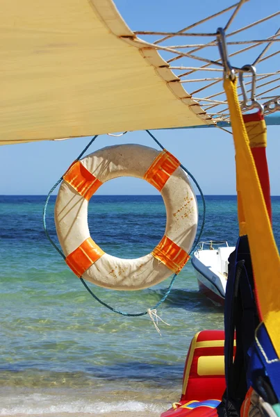 Boya salvavidas bajo un toldo blanco sobre un fondo de mar azul — Foto de Stock