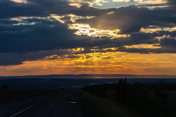 Black silhouettes of trees and a gray road are on a blue sky background with orange and yellow sunset — Stock Photo, Image