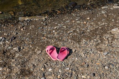 Bir çift pembe terlik, yaz günü göletin kenarındaki gri ve turuncu kırılan taşın güzel dokusunda bulunur.