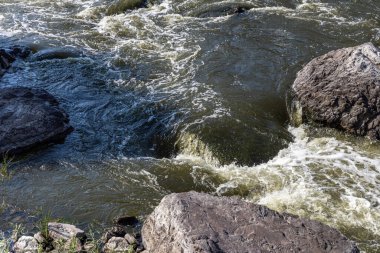 Yaz günü taşların arasında dalgalı bir dağ nehri akar.