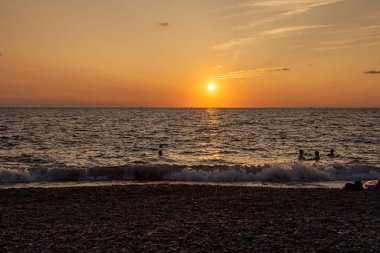 Sahilde güzel bir turuncu gün doğumu siyah gemi siluetleri ve yüzen bir grup insanla birlikte.