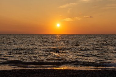 Sahilde güzel bir turuncu gün doğumu siyah gemi siluetleri ve yüzen bir grup insanla birlikte.