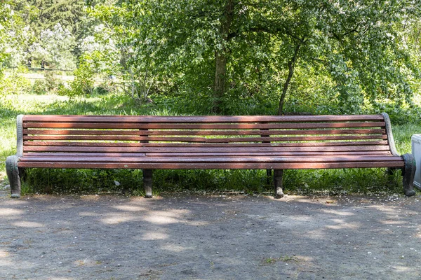 Antiguo banco de madera pintado de color marrón hermoso con patas de hierro forjado negro se encuentra junto a la pasarela en un parque — Foto de Stock