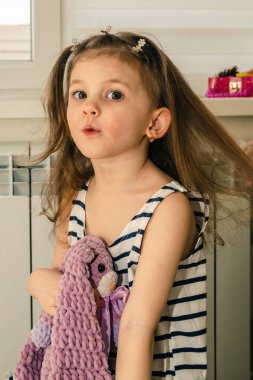 Küçük bir kız evde saçını yaptırırken oyuncağıyla oynuyor..