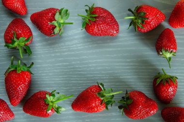 Gri ahşap arka planda bir sürü kırmızı olgun çilek..