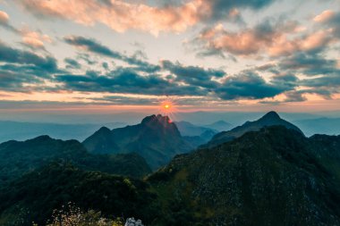 Gökyüzü, bulut ve güneş parıltılarıyla kaplı güzel dağ zirveleri