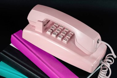 Siyah üzerine izole edilmiş bir kitap yığınının üzerindeki eski pembe telefonu kapat.