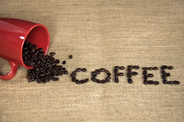 Coffee beans spilling out of red mug — Stock Photo, Image