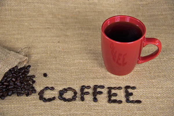 Kahve çekirdekleri ve çuval bezi üzerinde kırmızı kupa — Stok fotoğraf