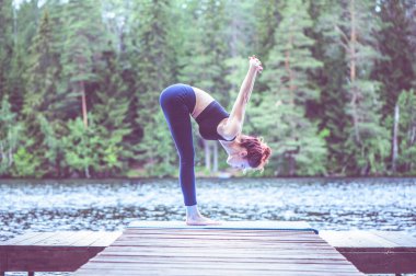 Genç bir kız gölde yoga yapıyor. Kadın mutluluğu. Sağlıklı yaşam ve doğal denge kavramı 