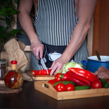 Önlüklü genç adam mutfakta yemek pişiriyor. Sağlıklı yiyecekler, yemek pişirme konsepti