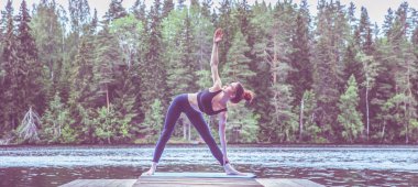 Yogi kızı yoga yapıyor, Utthita Trikonasana egzersizi yapıyor, gölde üçgen pozu veriyor. Sağlıklı yaşam ve doğal denge kavramı. Panoramik görünüm