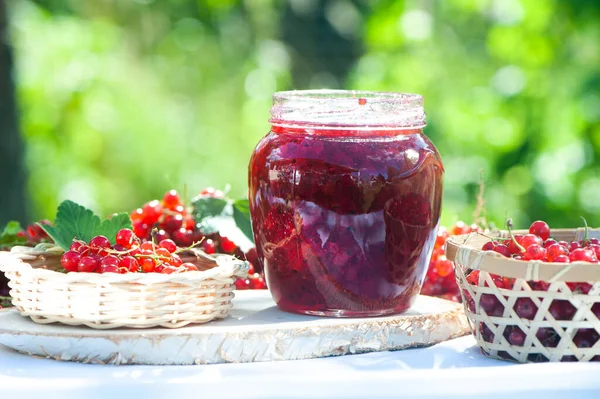 红醋栗的红色多汁浆果和浆果果酱在木制桌子上 花园的绿色背景上 收获和烹调的主题 — 图库照片