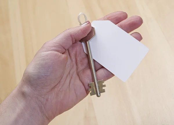 Tag attached to silver key in hand — Stock Photo, Image