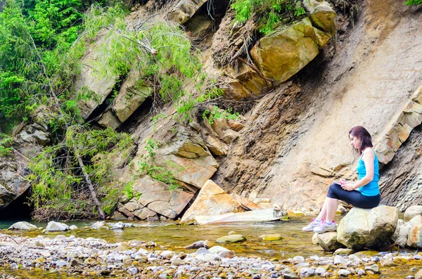 Bella ragazza siede su una roccia nel fiume e attinge da — Foto Stock