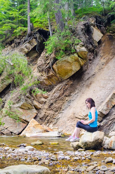 Bella ragazza siede su una roccia nel fiume e attinge da — Foto Stock