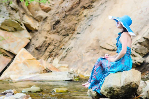 Beautiful young girl sits on a rock in the river and draws from — Stock Photo, Image