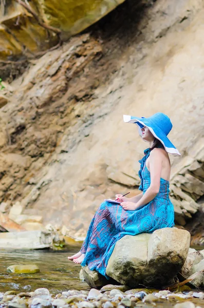 Beautiful young girl sits on a rock in the river and draws from — Stock Photo, Image