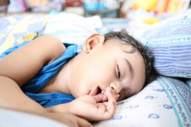 Bir dişi ağzında parmaklarıyla uyuyan sevimli Hintli bir bebek.