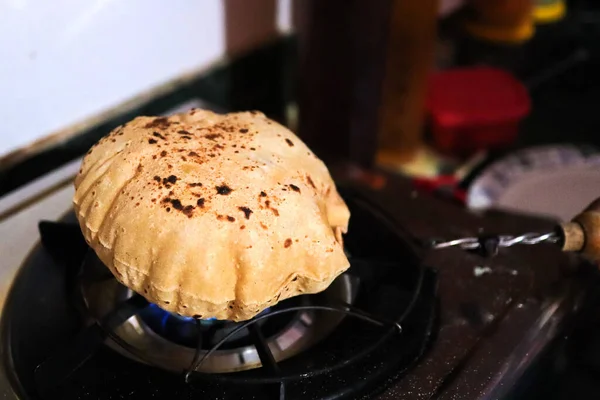 Nahaufnahme des Kochens eines Roti oder Chappati, der in der Küche auf einer blauen Gasflamme gebraten wird lizenzfreie Stockfotos