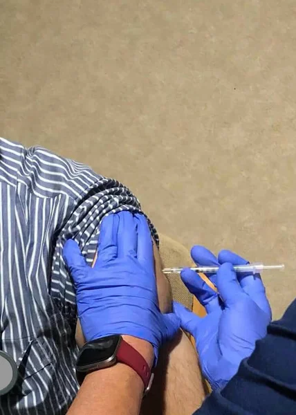 covid vaccine being given intra muscularly in the arm of a patient by blue gloved hand of a doctor