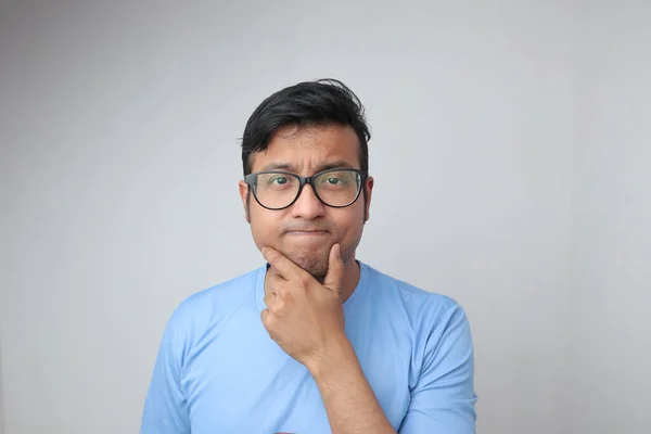 Un joven indio en gafas sosteniendo su barbilla y mirando confundido y reflexivo —  Fotos de Stock