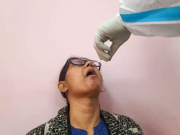 nasal swab being collected from a female suspected covid patient by a gloved hand of medical technician.