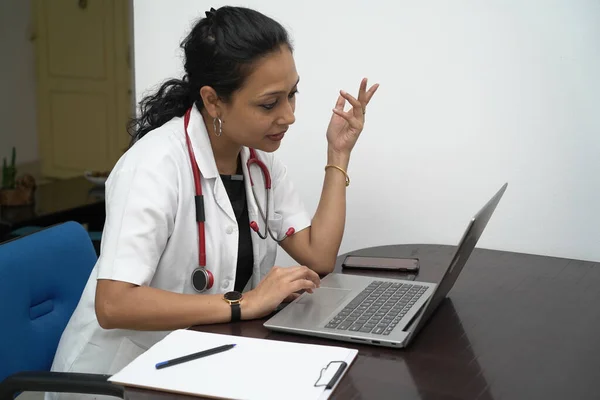 Un medico femminile indiano del sud negli anni '30 con laptop e scheda di prescrizione con cappotto bianco e stetoscopio rosso su sfondo bianco.Consulenza medica online — Foto Stock