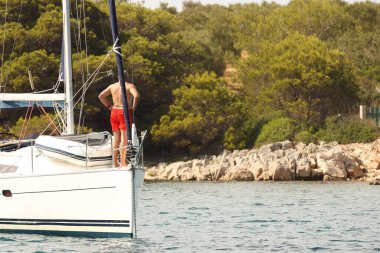 Kaptan yardımcısının eşi yatın nazusunda, çapa kapağının yanında. Yelkenli bir yatın demirlemesi. Denizde yaz tatili. Aktif yaşam tarzı. Suda ılımlı pembelik. Yat okulu. Gemi Mürettebatı Qua