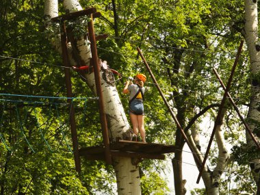 Yaslo, Polonya - 872019: Genç bir kız kaya tırmanışı için parktaki ağaçlara tırmanıyor. Spor etkinlikleri için İskandinav cazibesi. İp sigortası ve koruma araçları. Yükseklikte güvenlik.