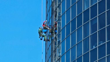 İki dağcı büyük bir yükseklikte bir gökdelenin dış camlarını siler. Ulaşılması zor yerlerin profesyonel temizliği. Para kazanmada spor becerileri