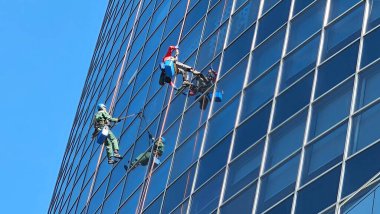 İki dağcı büyük bir yükseklikte bir gökdelenin dış camlarını siler. Ulaşılması zor yerlerin profesyonel temizliği. Para kazanmada spor becerileri