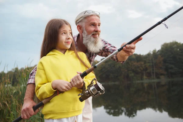 湖で孫娘の釣りを教えるのを楽しんでいる幸せな高齢者 コピースペース — ストック写真