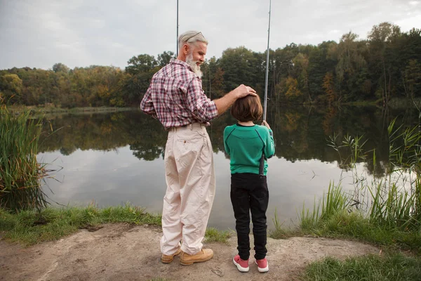 後ろのビュー湖で彼の孫釣りを見て誇りに思っておじいちゃんの完全な長さのショット — ストック写真