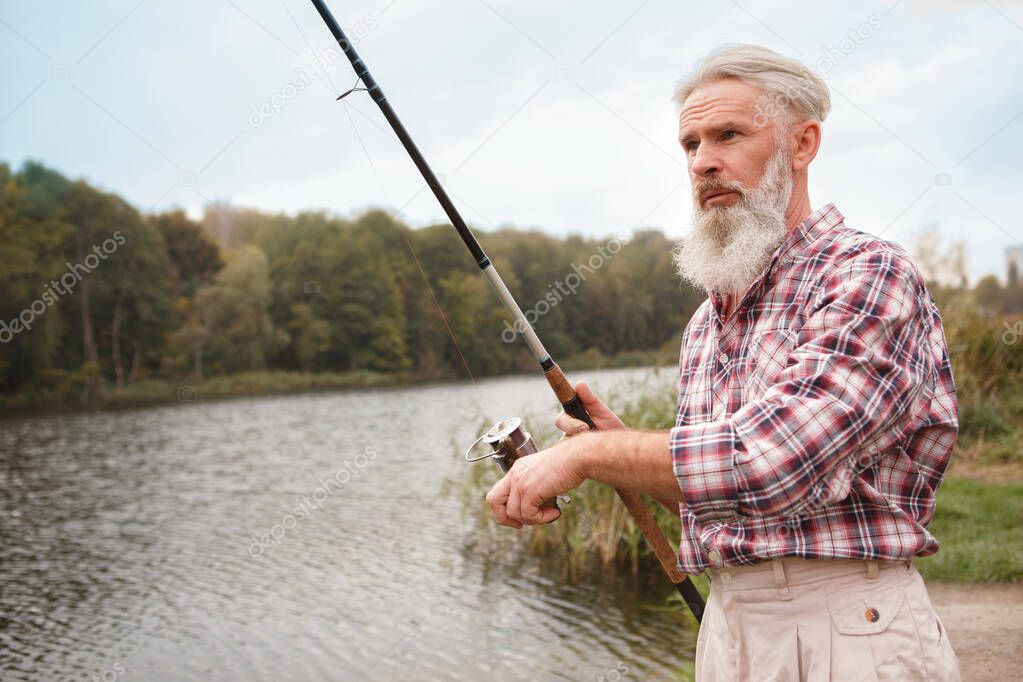 Senior bearded man fishing on a lake, copy space