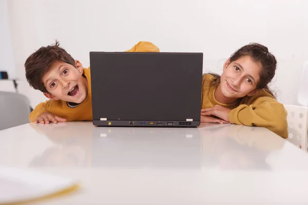 快乐的兄妹对着摄像机笑着 从他们的笔记本电脑里窥视着 复制着空间 — 图库照片