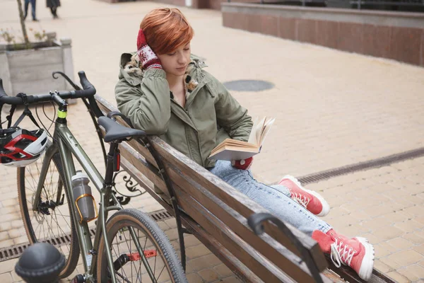 Young female student reading a book, relaxing after riding bicycle in the city