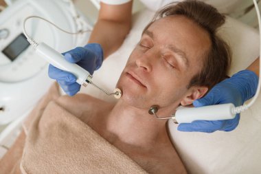 Kozmetik uzmanının cilt bakımının keyfini çıkaran rahat olgun bir adamın üst görüntüsü.