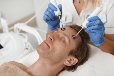 Güzellik salonunda elektroliz yüz bakımı gören bir erkek hastaya yakın çekim