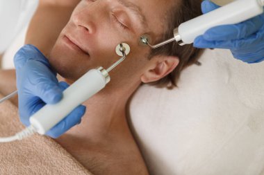 Yetişkin bir erkek müşterinin güzellik kliniğinde yüz elektrolizi ameliyatı olurken görüntüsü.