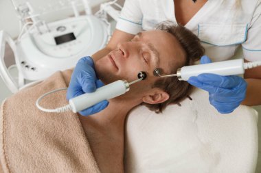 Erkek müşteriye elektroliz yüz prosedürü uygulayan tanınamayan bir kozmetikçi.