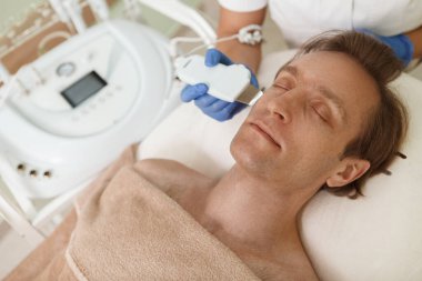 Close up of a mature man relaxing at beauty clinic, getting facial ultrasound  procedure