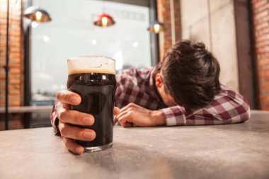 Barda uyuyan sarhoş adamın elindeki bira bardağına odaklan.