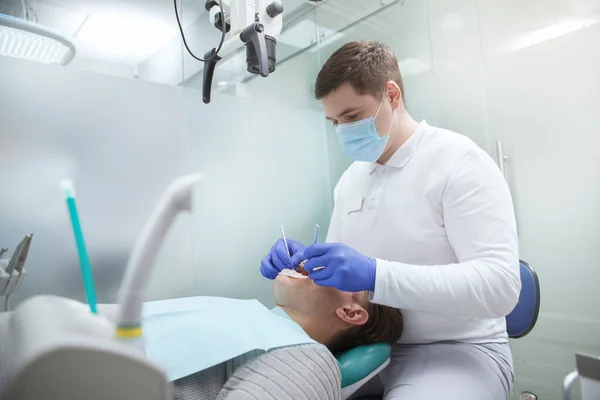 Profesjonalny Dentysta Pracujący Klinice Leczący Zęby Męskiego Pacjenta — Zdjęcie stockowe