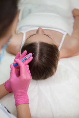 Kozmetik uzmanları tarafından saç dökülmesi tedavisi gören bir kadının dikey çekimi.