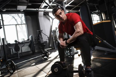 Halterlerle çalıştıktan sonra dinlenen kaslı, güçlü bir sporcunun düşük açılı çekimi.